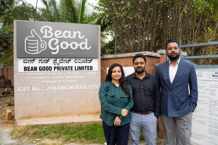 Two men and one woman stand in front of a 'Bean Good Indian Brewed Coffee' sign.