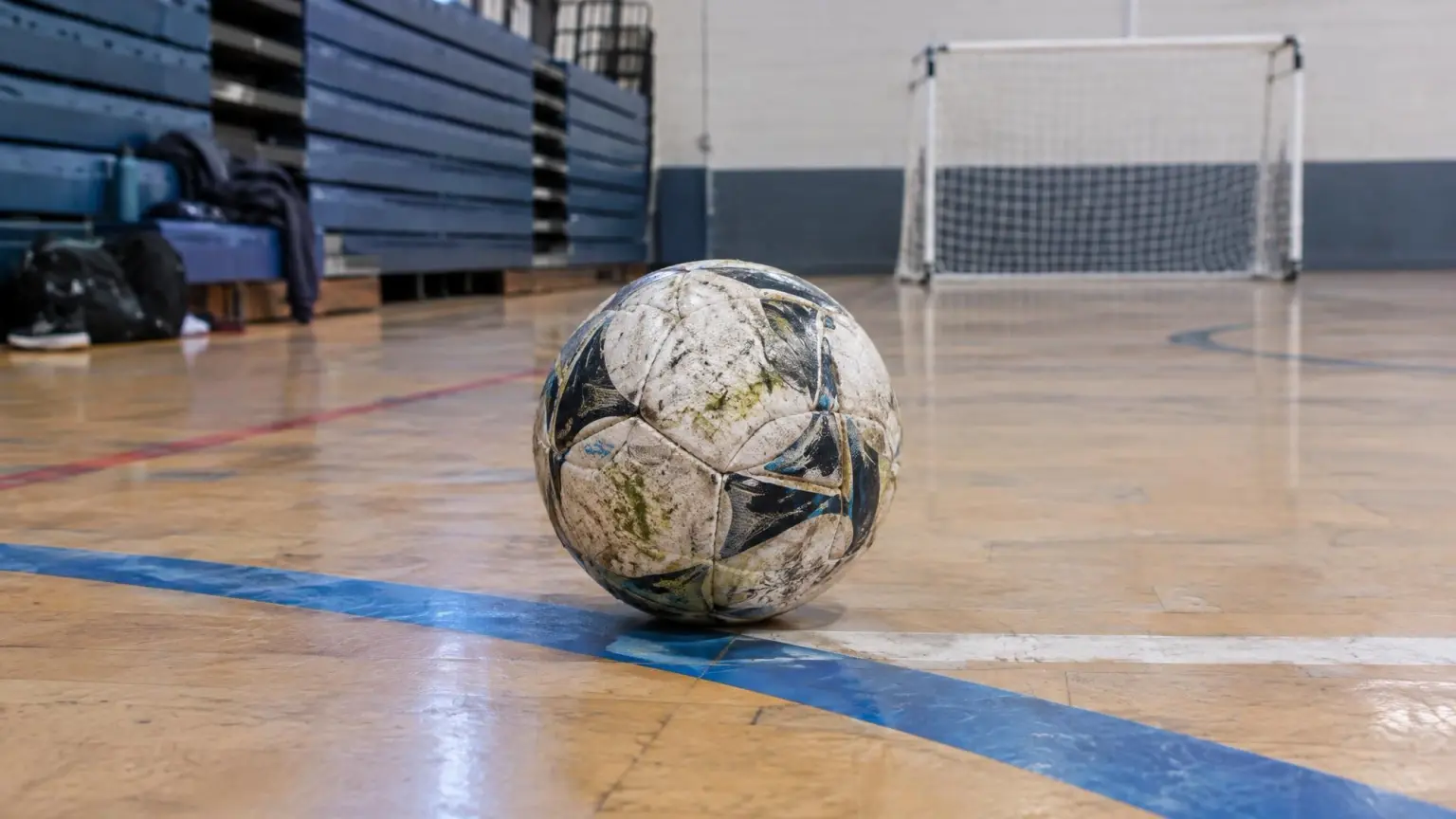 A low-bounce futsal ball resting on the painted lines of a school gymnasium floor, the hard indoor court futsal is played on.