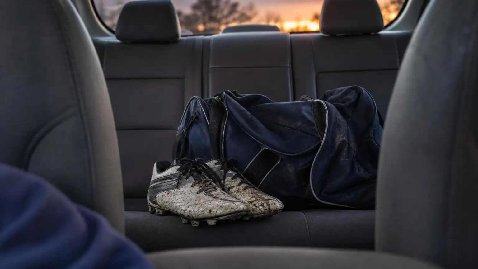 A youth soccer bag and muddy cleats on a car back seat at dusk, the setting for what to say to your child after a soccer game