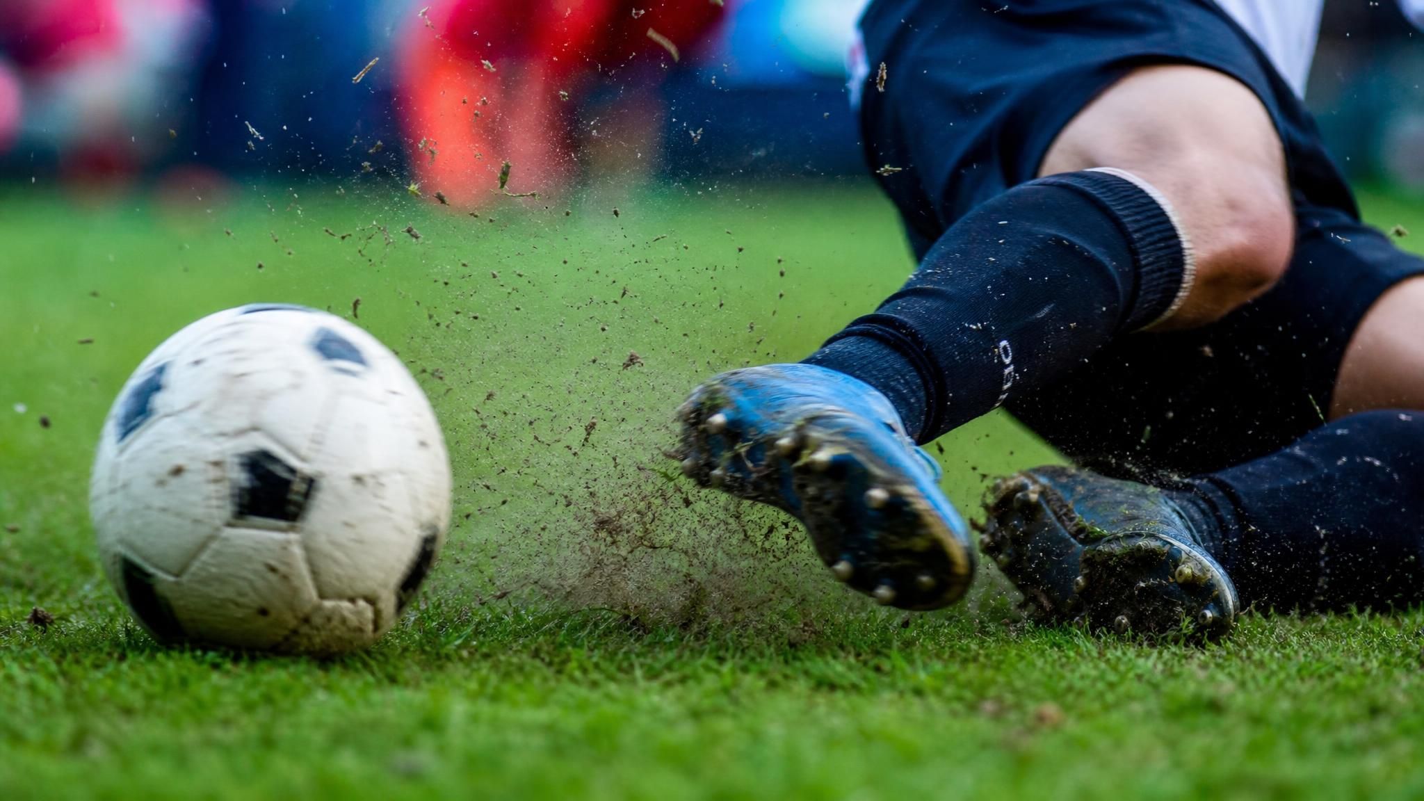 A youth soccer player sliding low across wet grass toward the ball, illustrating slide tackle rules in soccer