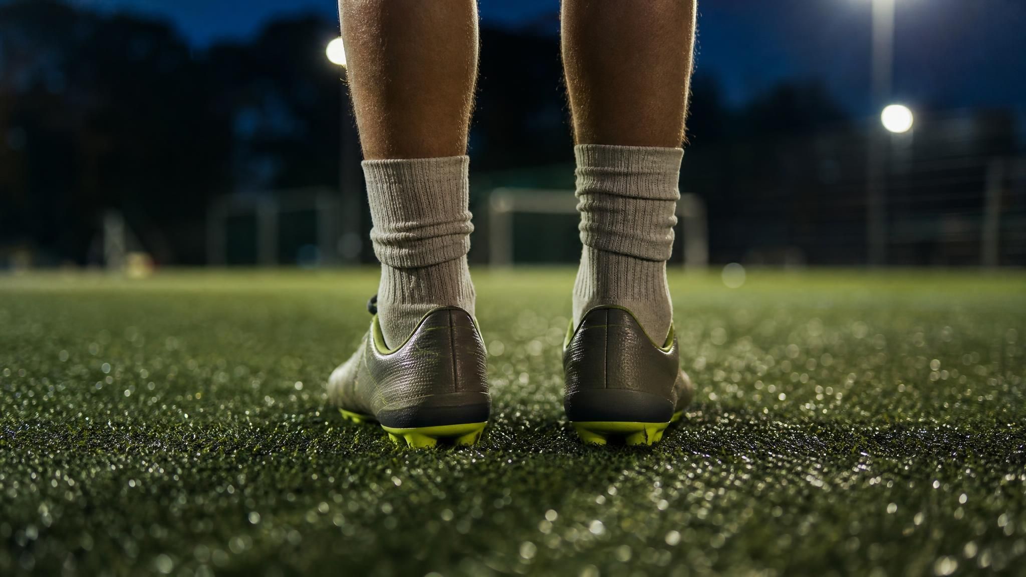 Close-up of a young soccer player's lower legs in socks and cleats on floodlit artificial turf, illustrating shin splints in youth soccer