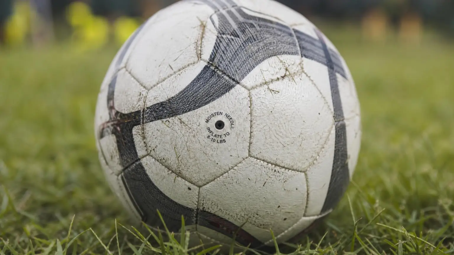 Close-up of a worn soccer ball on grass showing the valve and printed inflation pressure marking, illustrating how to read FIFA quality marks and specs on a soccer ball