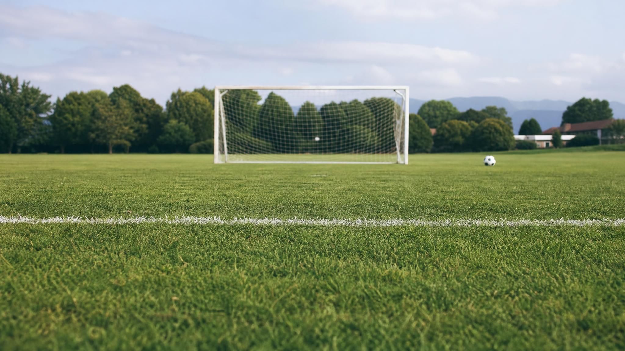 A painted white build-out line running across a green grass youth soccer field with a small goal in the background, illustrating the build-out line in 7v7 soccer