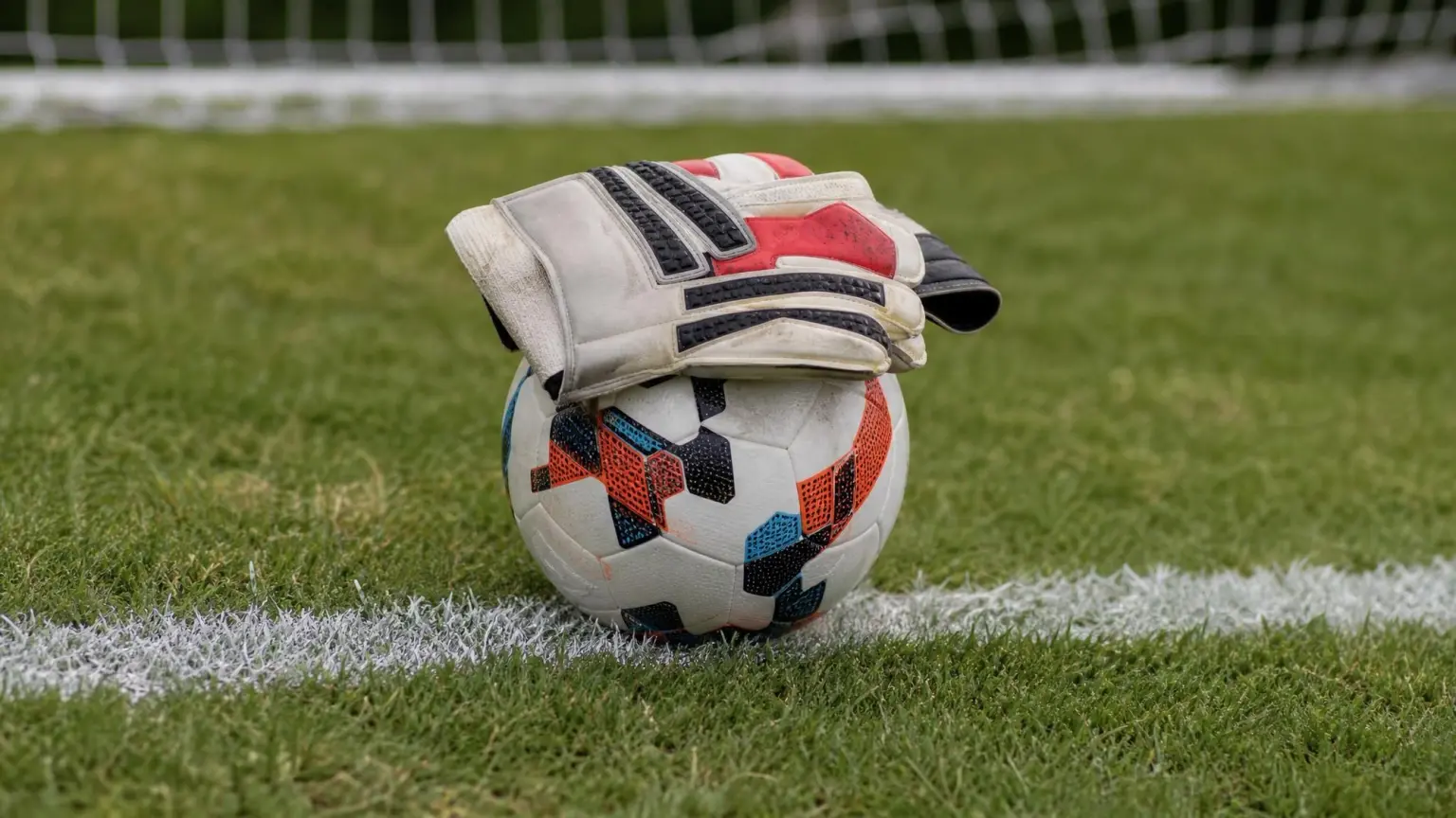 A youth soccer goalkeeper's gloves resting on the ball inside the penalty area, illustrating the back-pass rule and when a goalkeeper can handle the ball