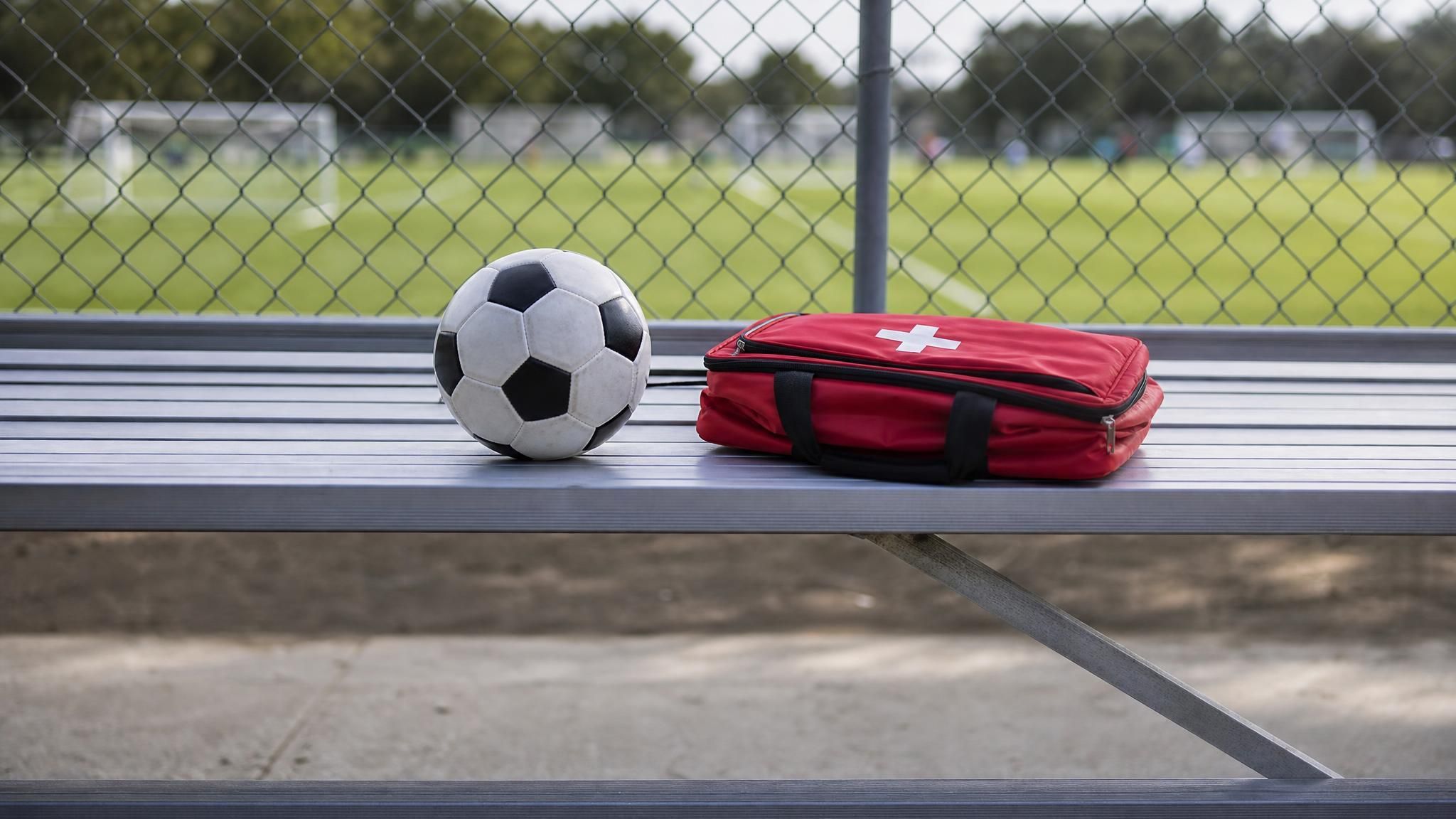 An empty youth soccer sideline bench with a ball and a medical kit bag, representing the youth soccer concussion protocol and removal from play