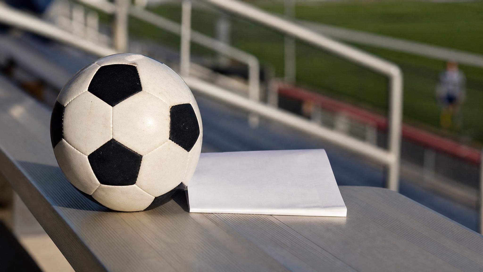 A soccer ball resting next to a folded recruiting letter on empty stadium bleachers, representing the college soccer recruiting timeline