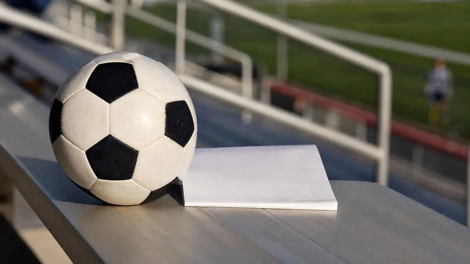 A soccer ball resting next to a folded recruiting letter on empty stadium bleachers, representing the college soccer recruiting timeline