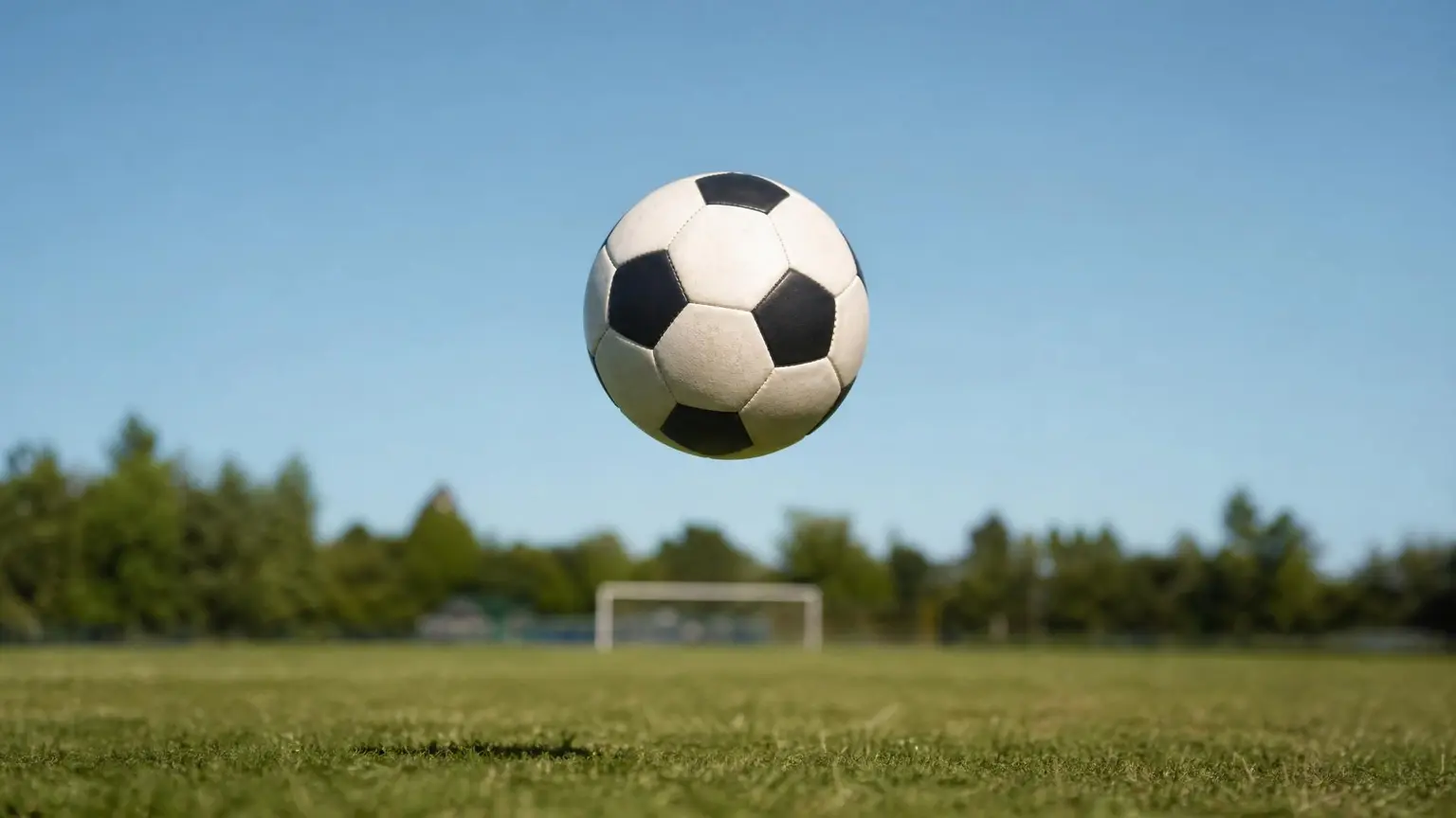 A soccer ball frozen in mid-air above an empty youth soccer field, illustrating youth soccer heading rules and when kids can head the ball