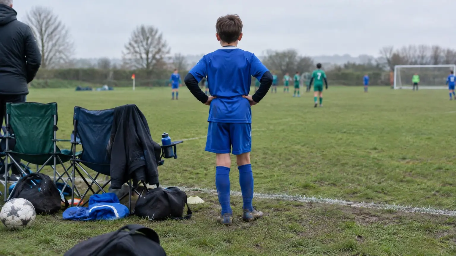 A young soccer player waiting on the touchline of a grass field before going on, illustrating why a child may play better in practice than in games
