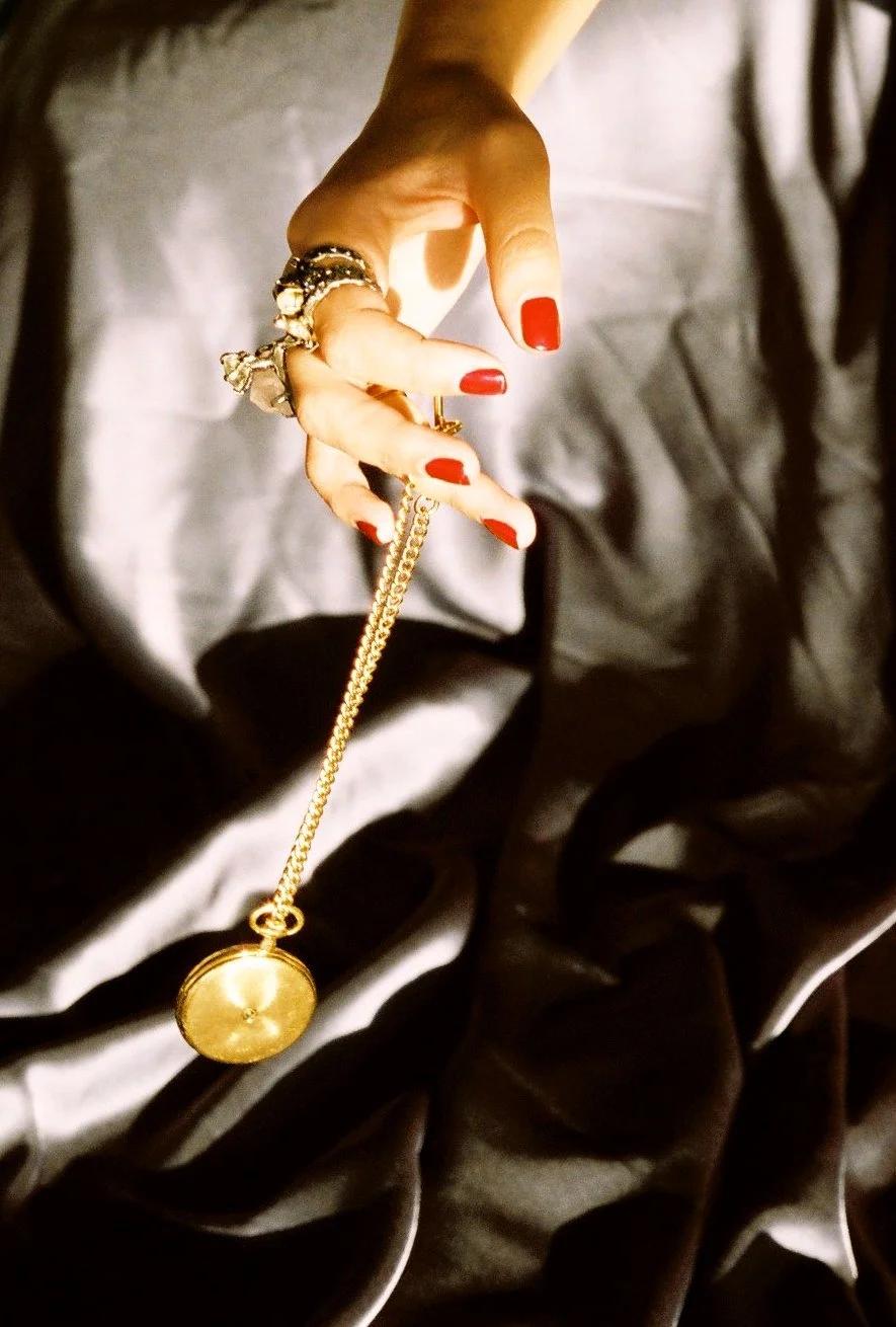 Ringed hand with red nails holds a gold pocket watch