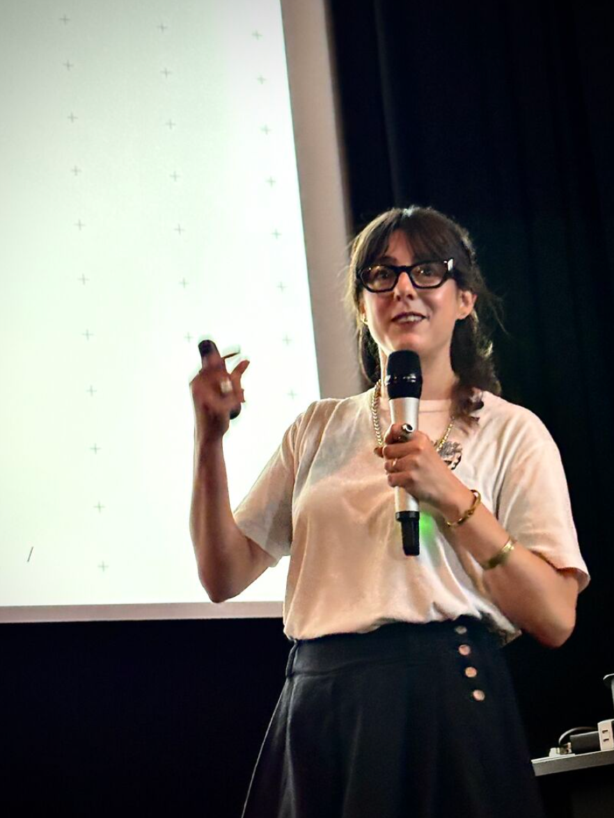 Woman speaks into a microphone beside a presentation screen
