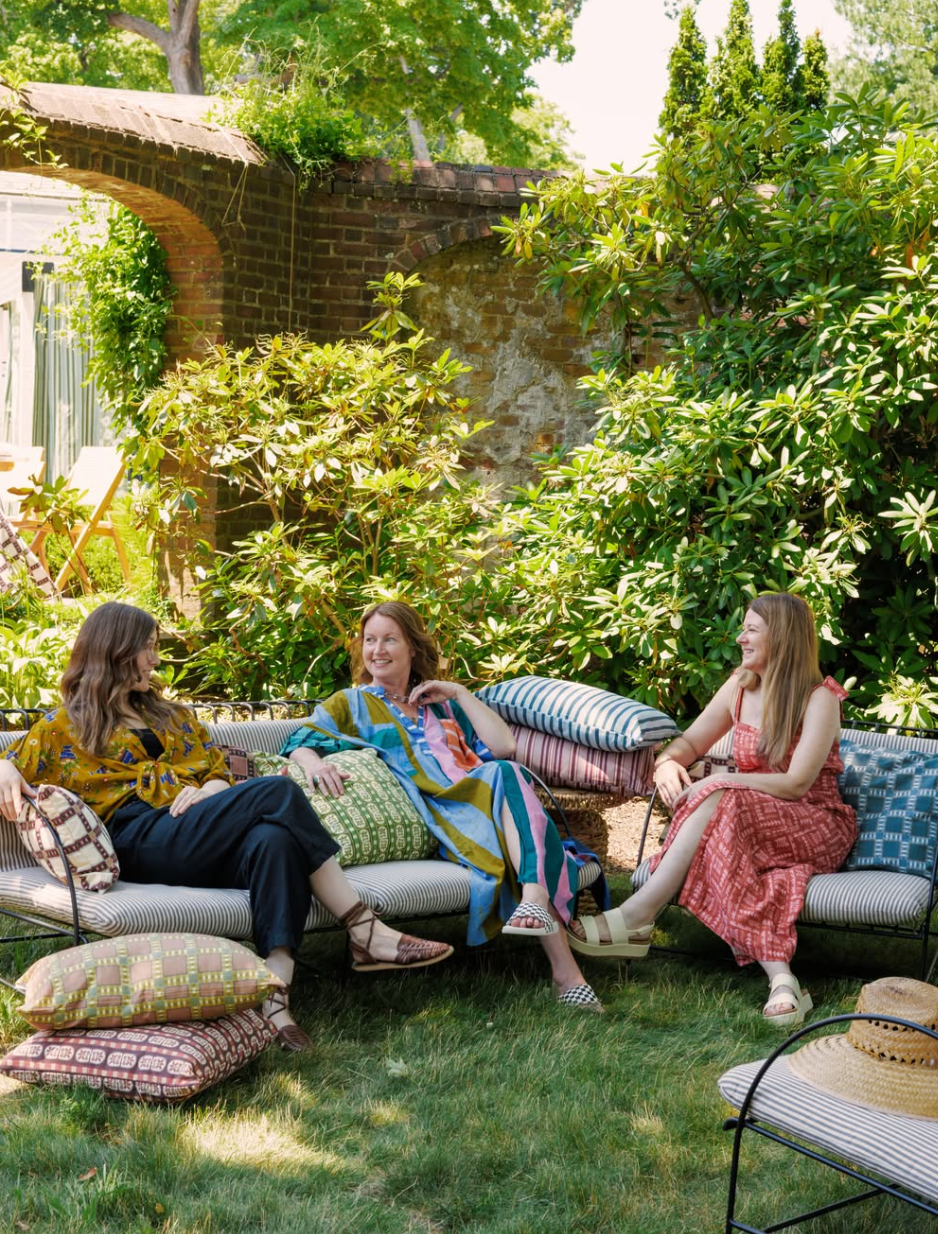 Three women sit together and talk in a garden