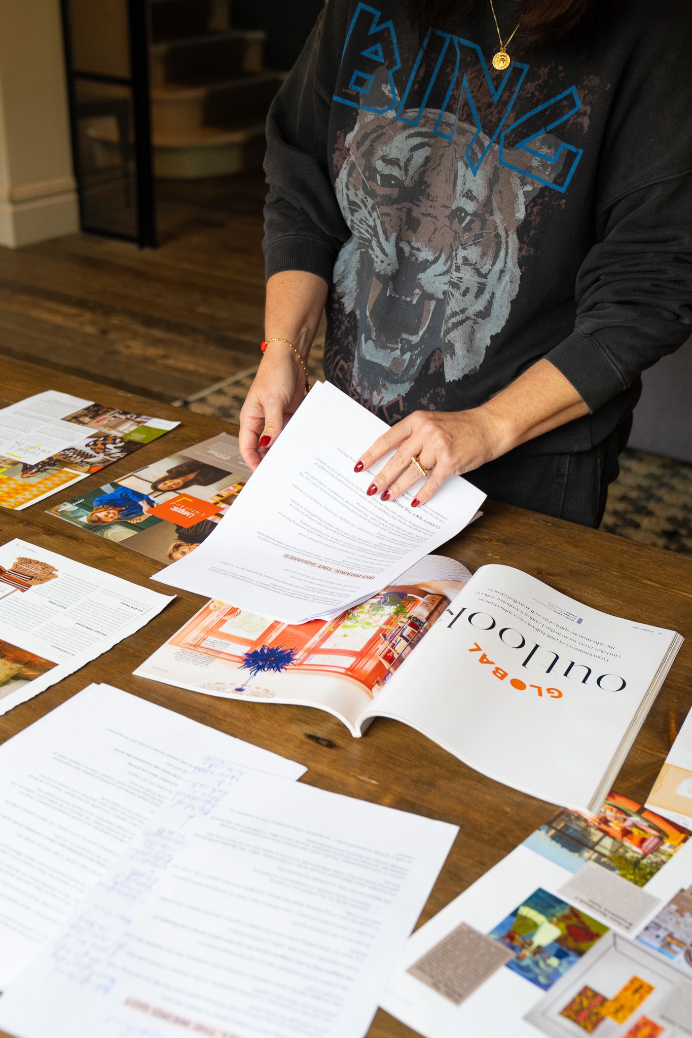 Person reviews printed documents and magazines spread across a table