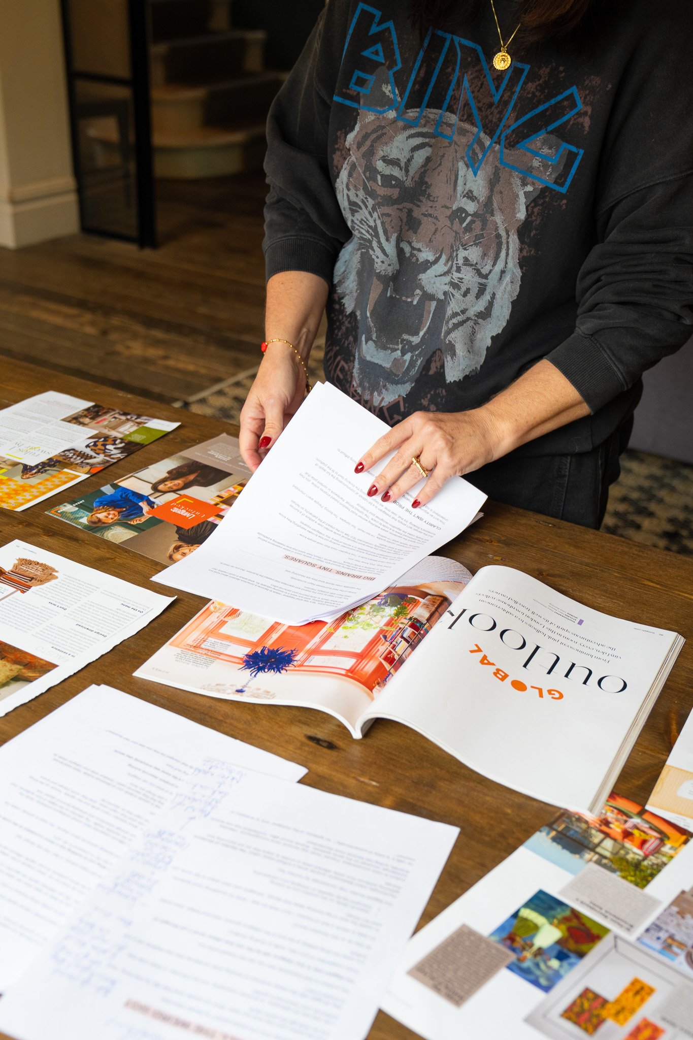 Person reviews printed documents and magazines spread across a table