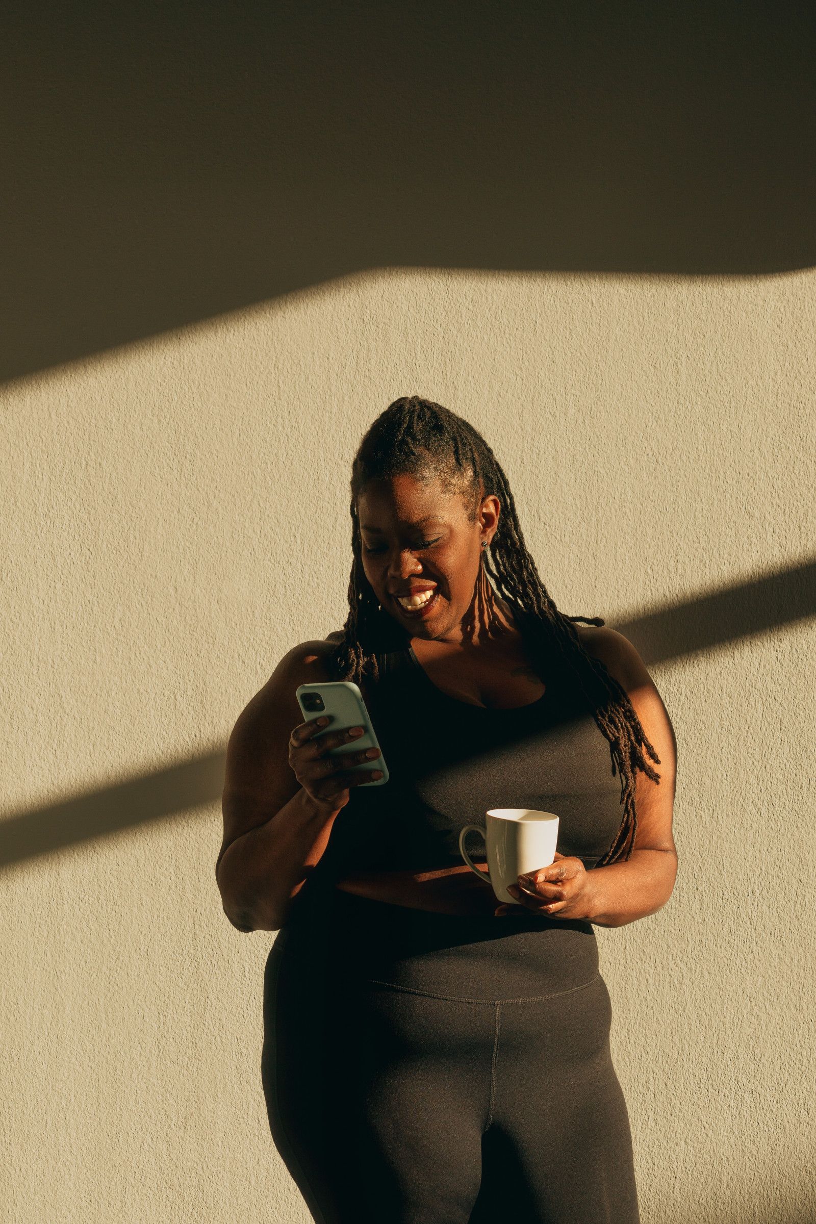 Woman smiles at her phone while holding a mug