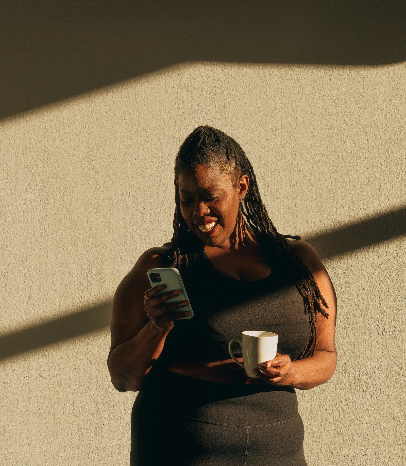 Woman smiles at her phone while holding a mug