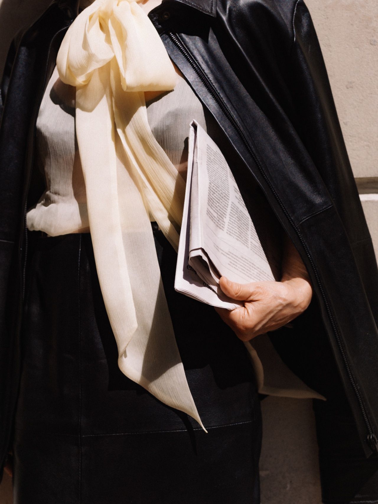 Person in a leather jacket and scarf holding a folded newspaper