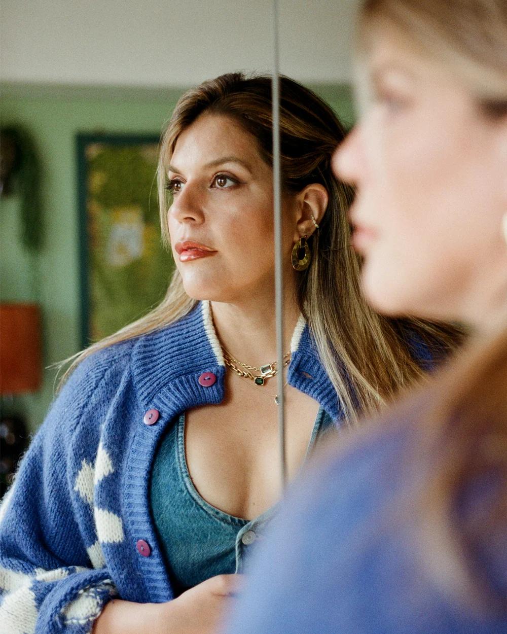 Woman in a blue cardigan looks into a mirror