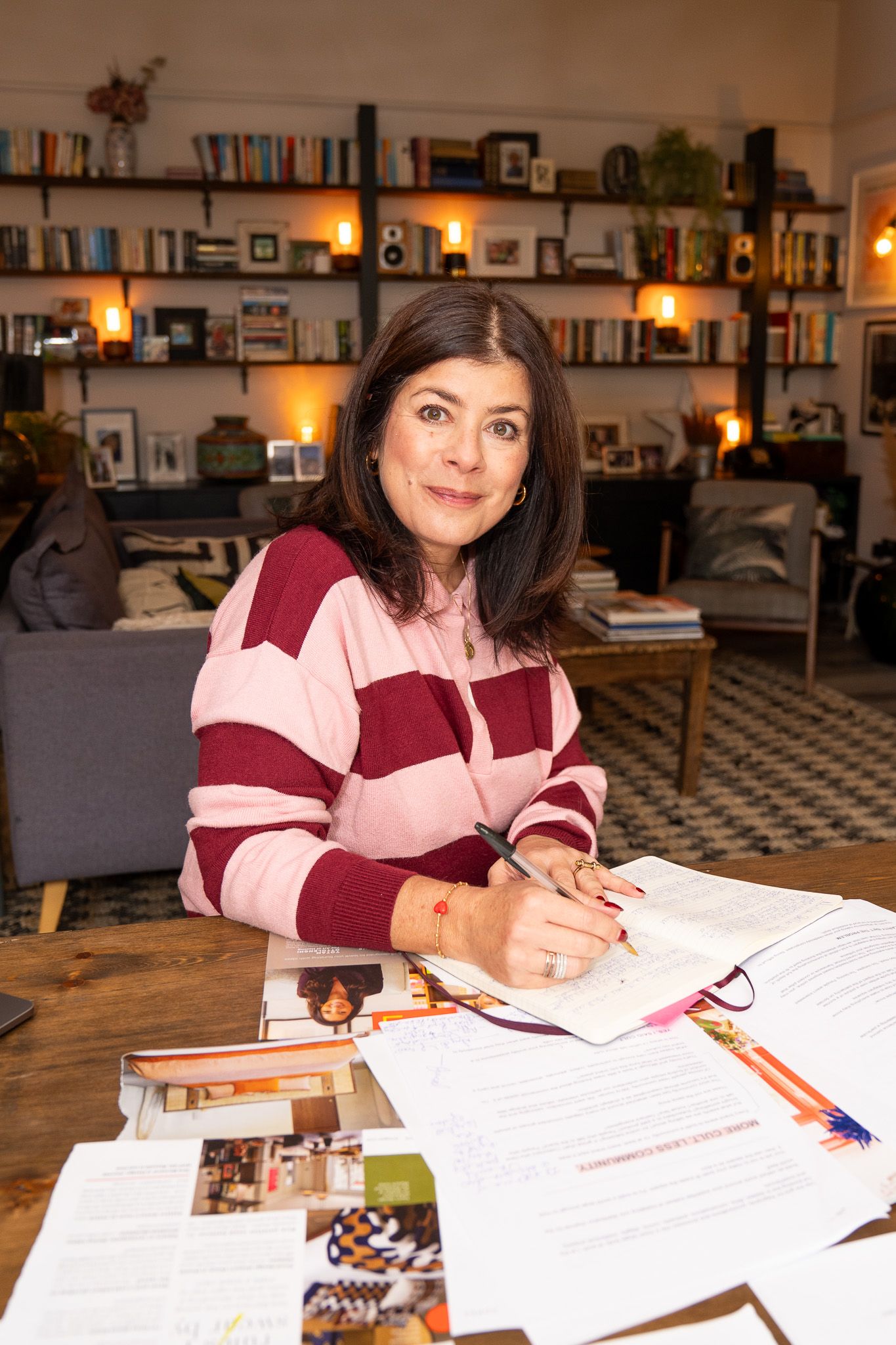 Woman writing in a notebook at a table covered with documents