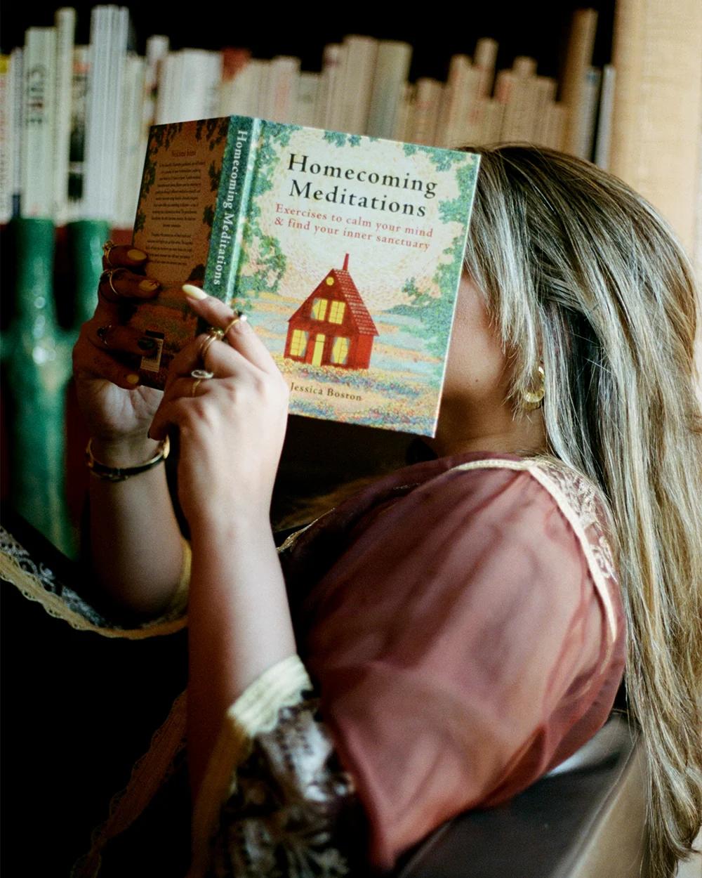 Woman reads “Homecoming Meditations” in front of a bookshelf
