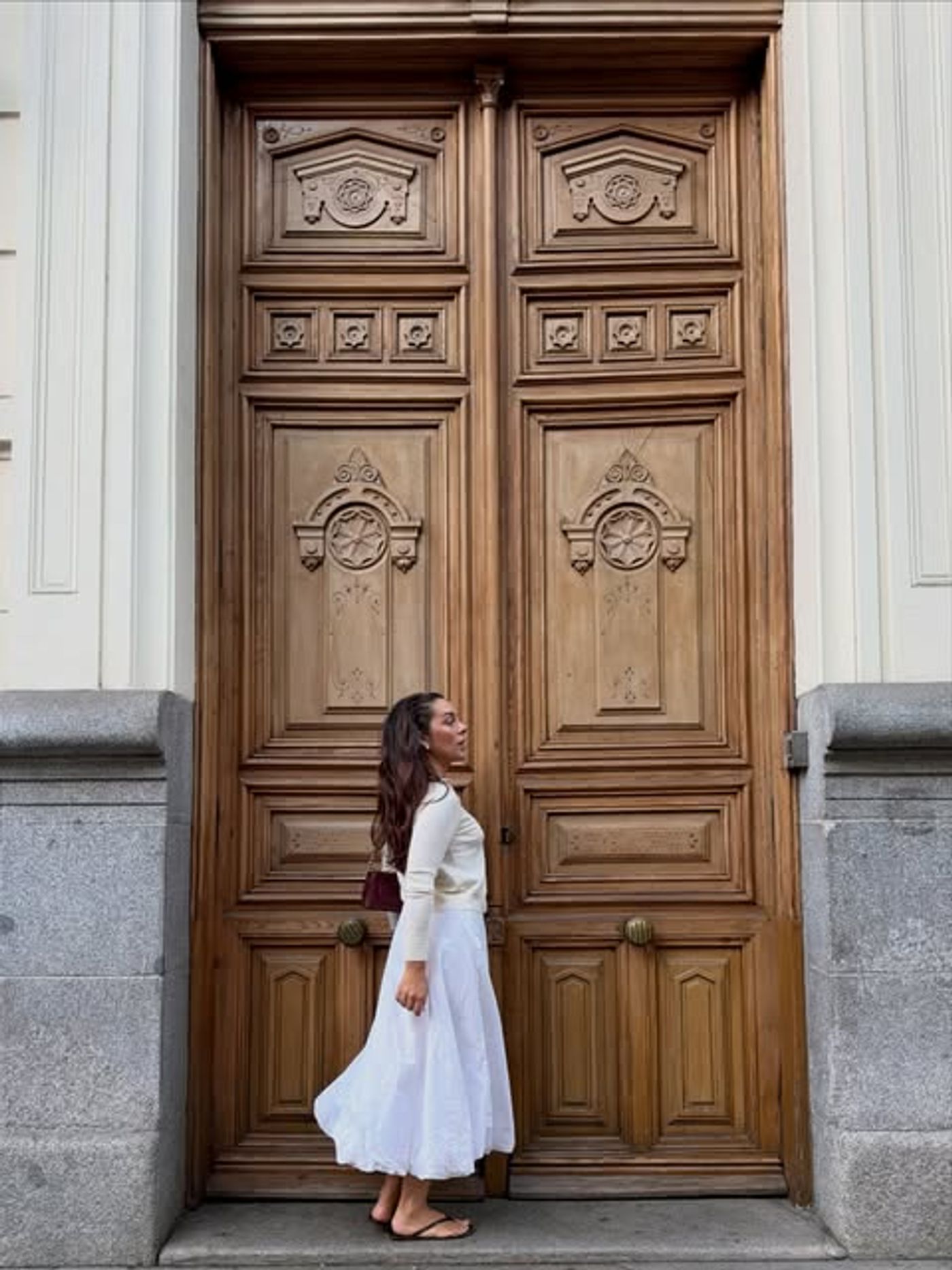 Mujer con vestido blanco frente a una puerta de madera tallada