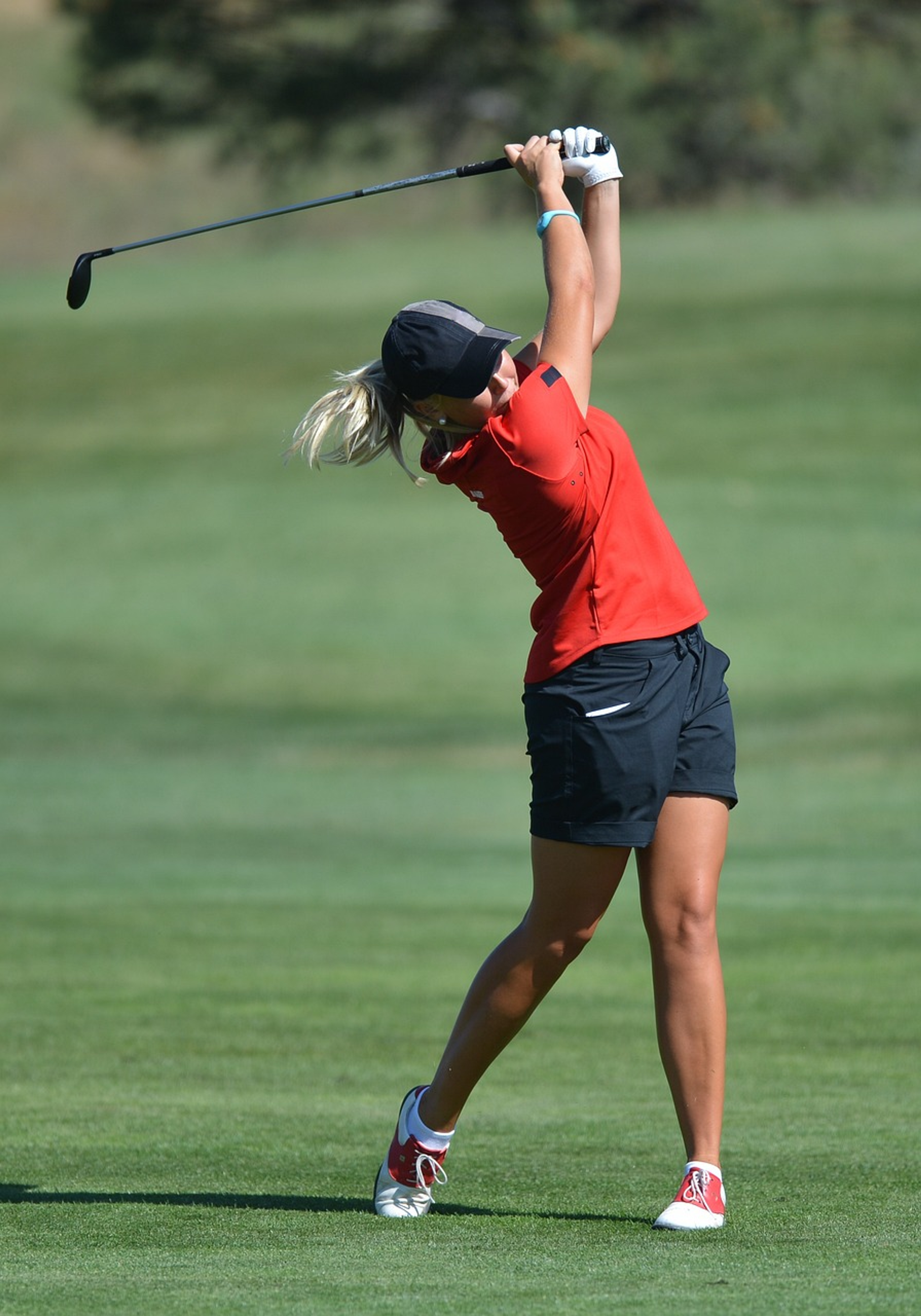 Female college golfer in action, swinging at golf ball with focus and precision.