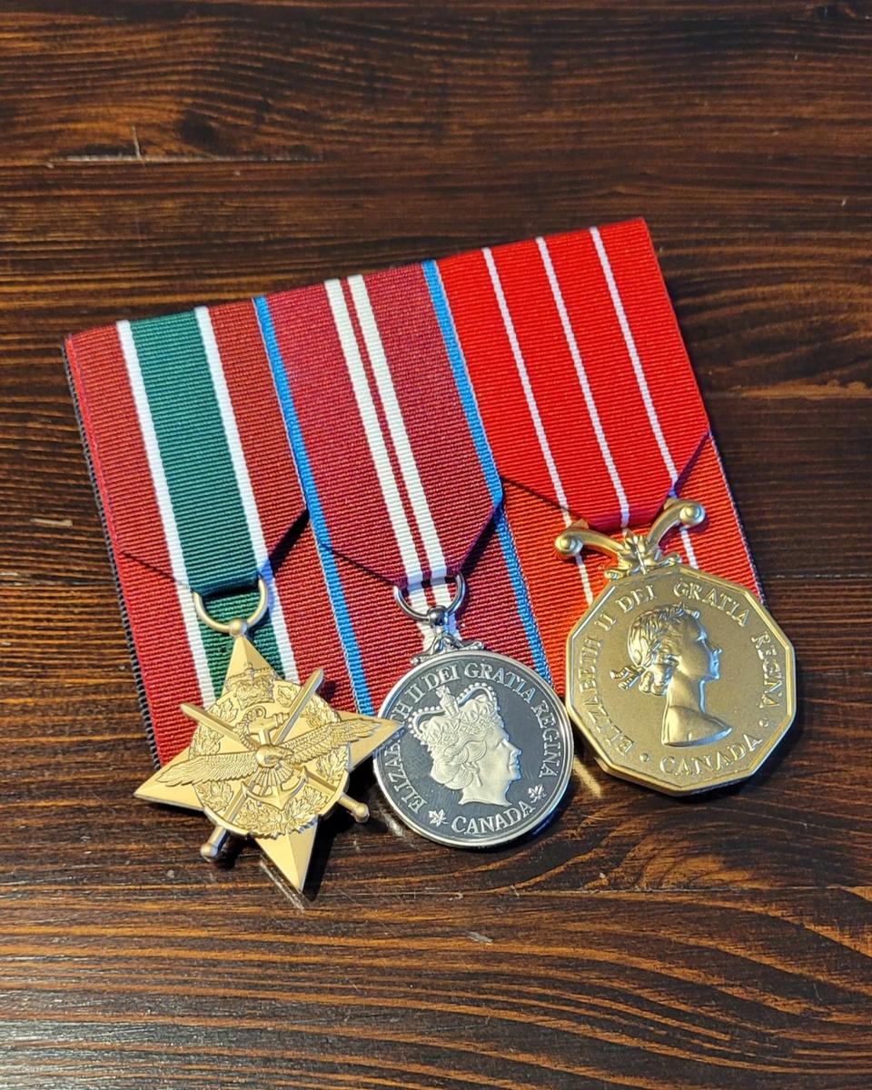 A court-mounted trio of full-size Canadian service medals on a wood table