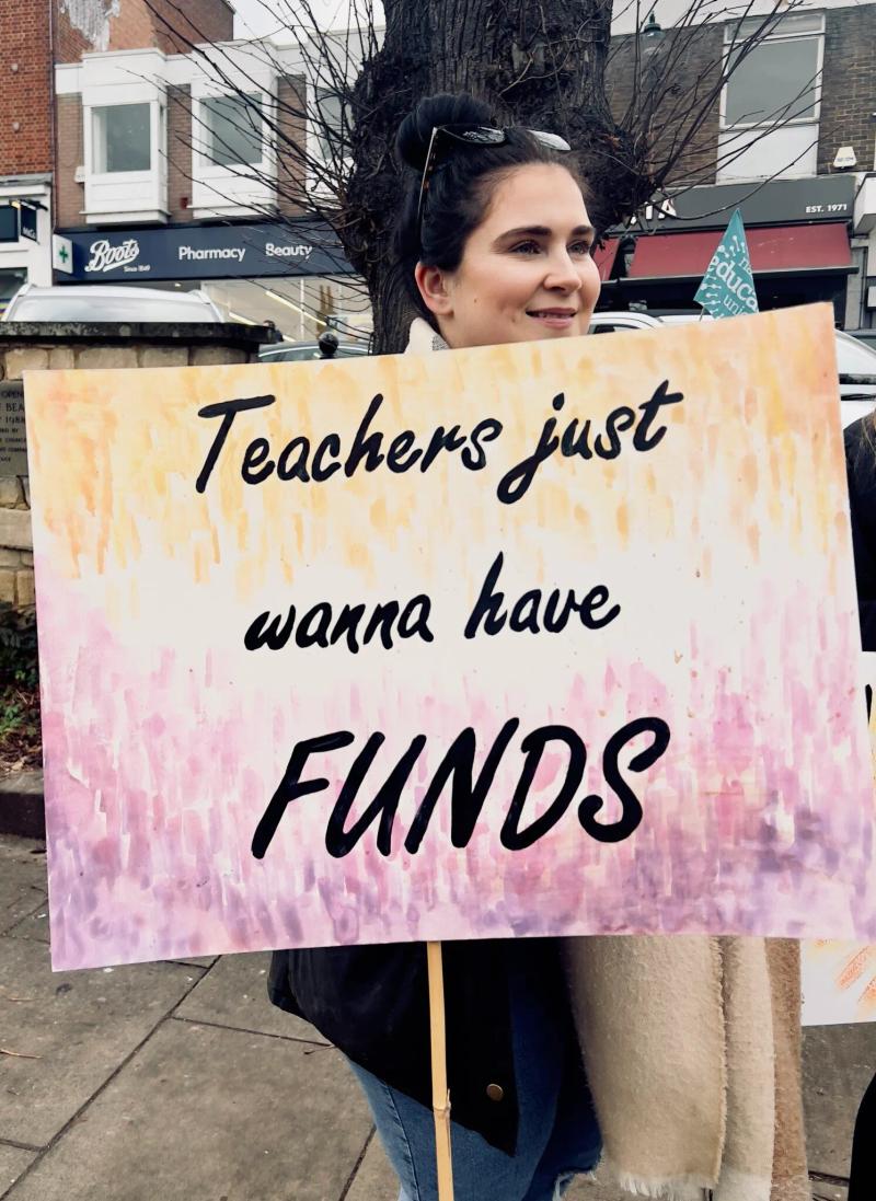 teacher holding protest sign that says teachers just wanna have funds