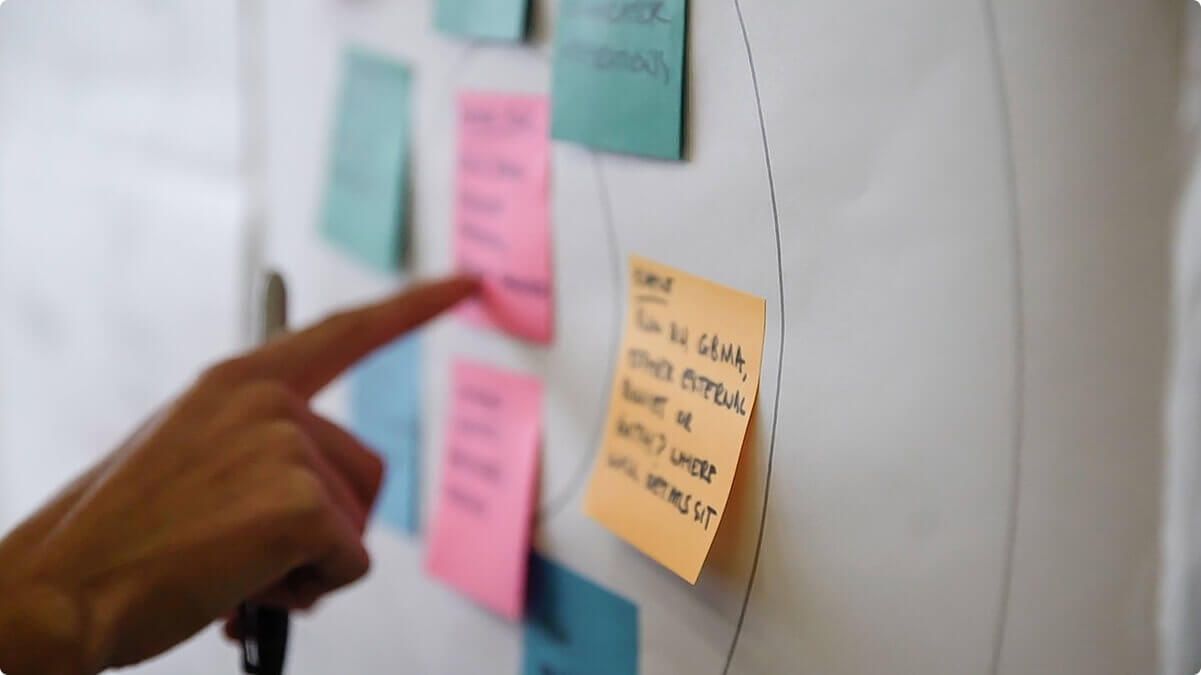 The hand of an Airteam team member pointing at a post it note on a wall.