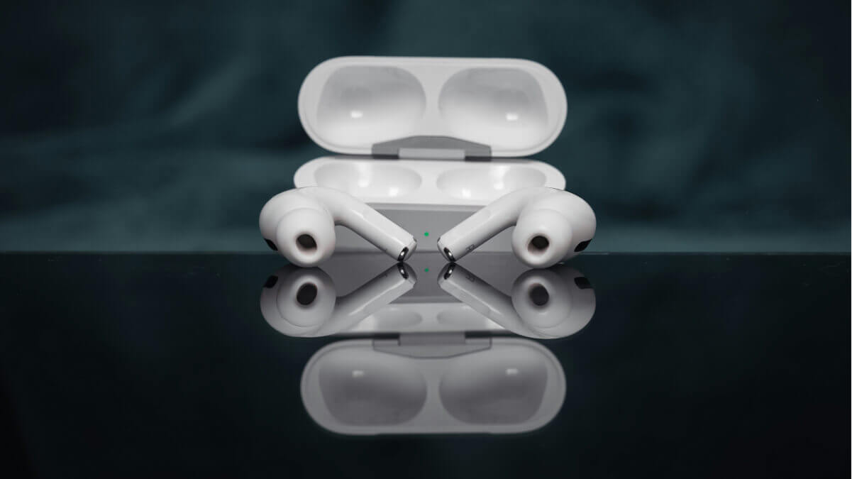A pair of wireless white earbuds with silicone tips resting on a reflective black surface, positioned in front of an open cha