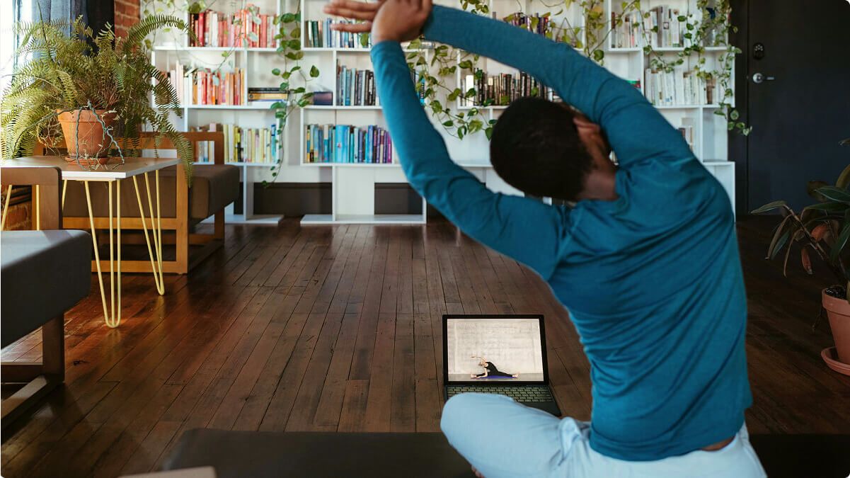 Person in a green long sleeve top stretching on a yoga mat at home.