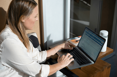 A woman sitting at her desk in front of a laptop being handed a contract.