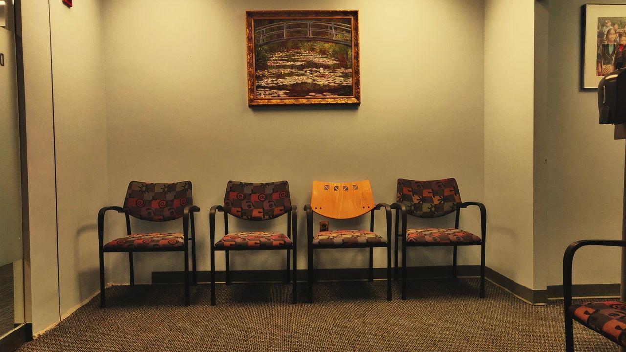 An empty hospital waiting room with a row of chairs under warm light
