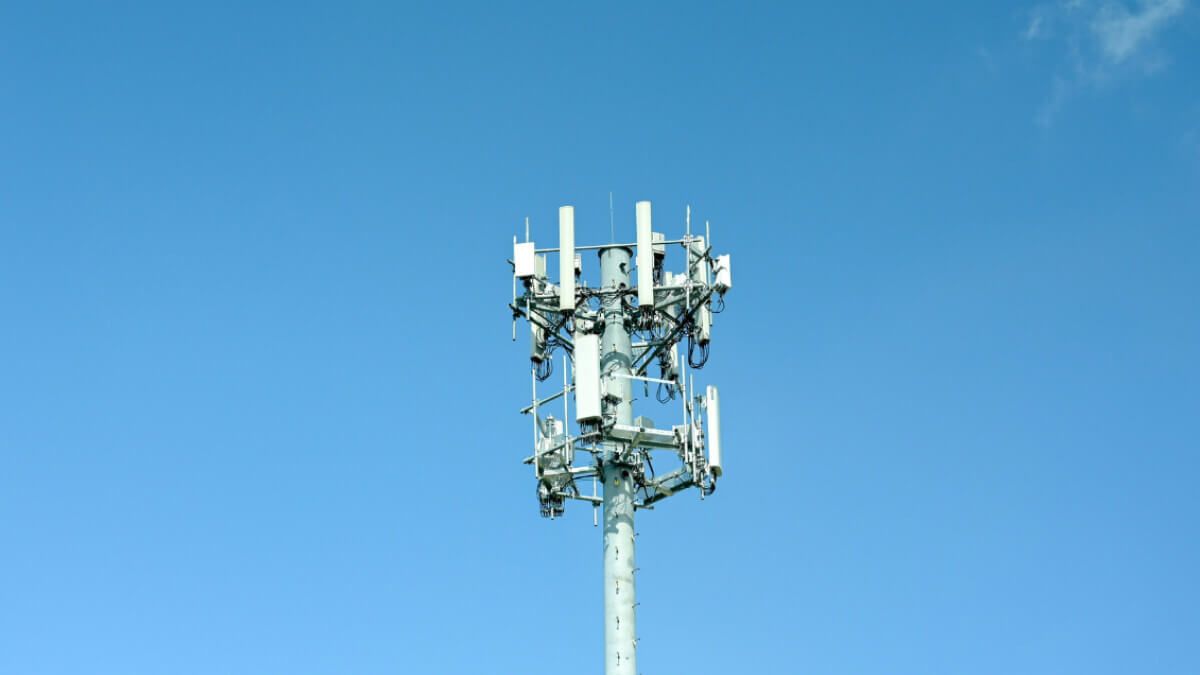 A mobile phone tower with multiple antennas against a clear blue sky.