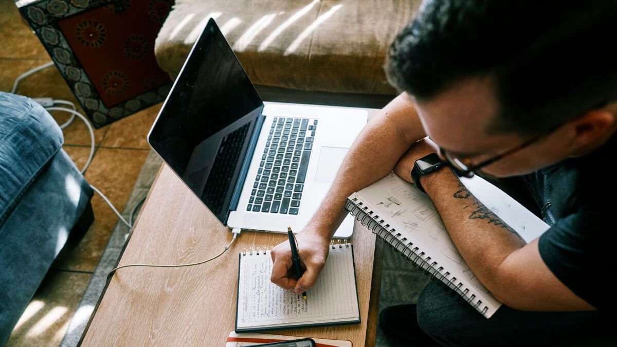 Person writing notes beside a laptop, analysing data for a research report.