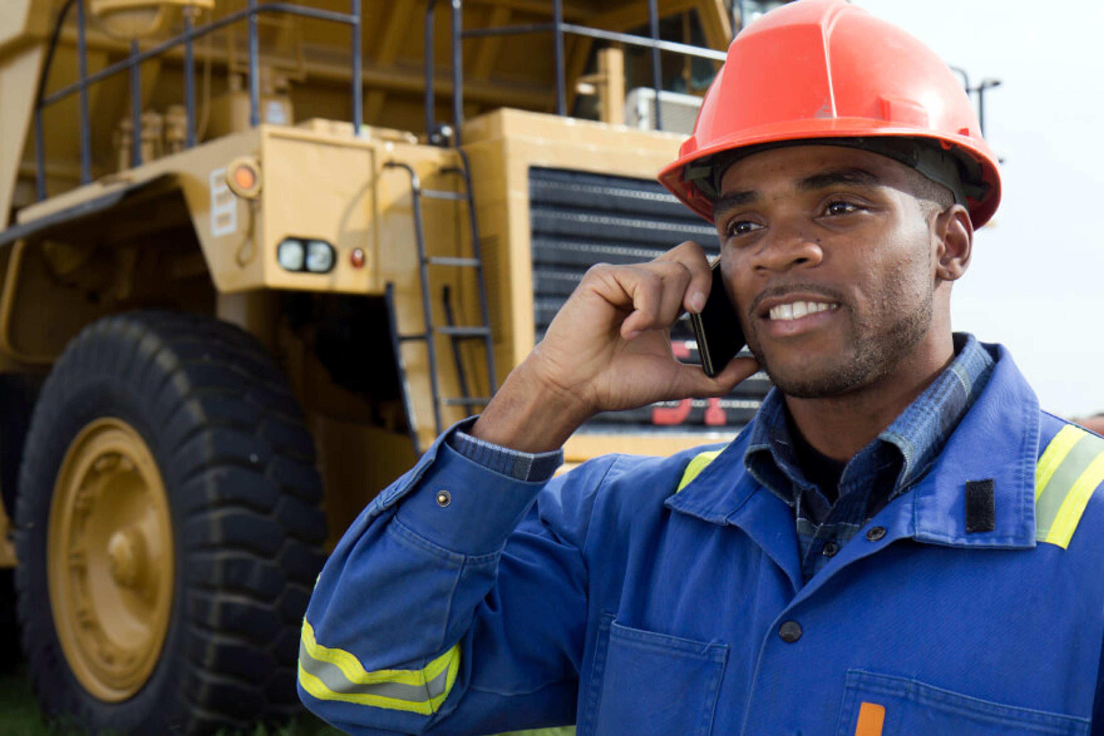 A miner using a mobile phone in front of a dump truck