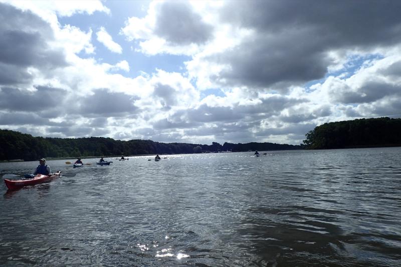 Weite Wasserfläche mit Kajaks vor dramatischen Wolken.