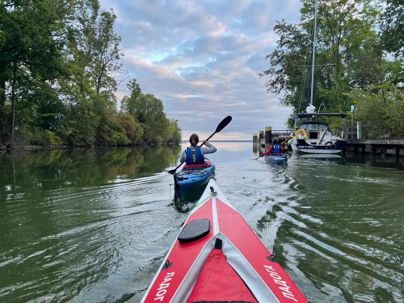 Paddlerin im Kajak auf dem Weg zur Müritz, rechts ein Segelboot am Steg.