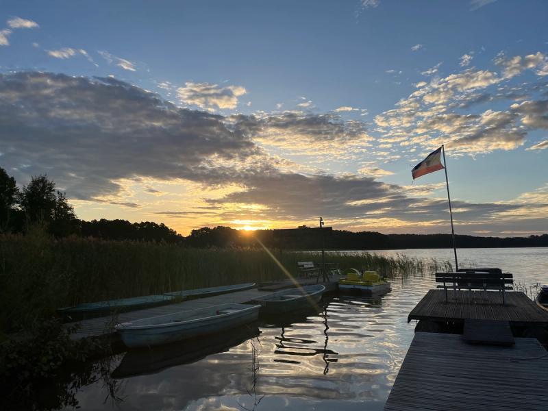 Sonnenaufgang über einem See mit Steg und Booten.