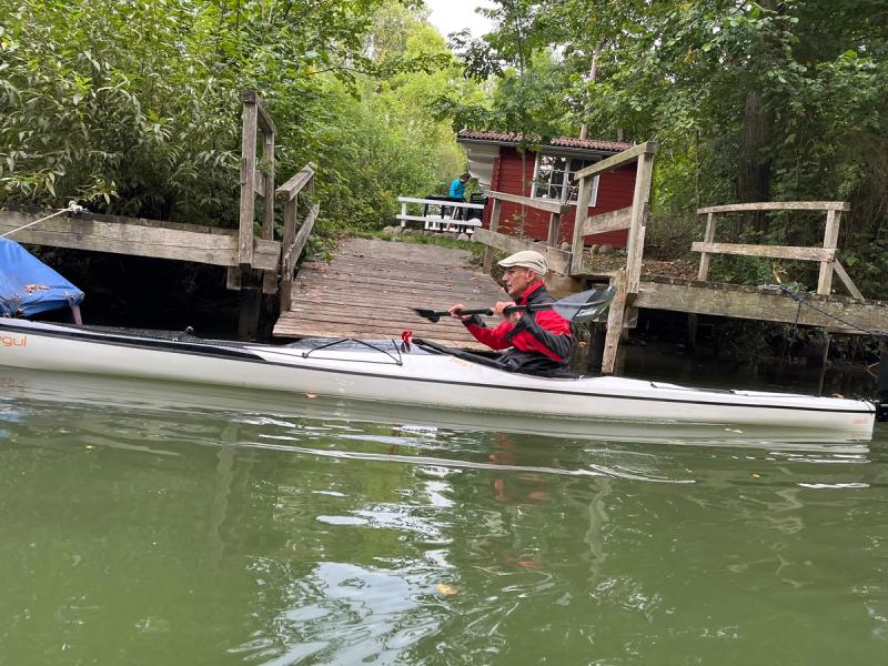 Paddler im weißen Kajak vor einem Steg mit roter Hütte.