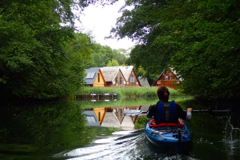 Paddlerin fährt in einem Kanal auf Ferienhäuser am Wasser zu.