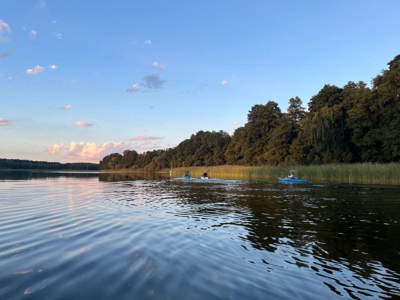 Abendlicht über einem ruhigen See, in der Ferne zwei Kajaks.