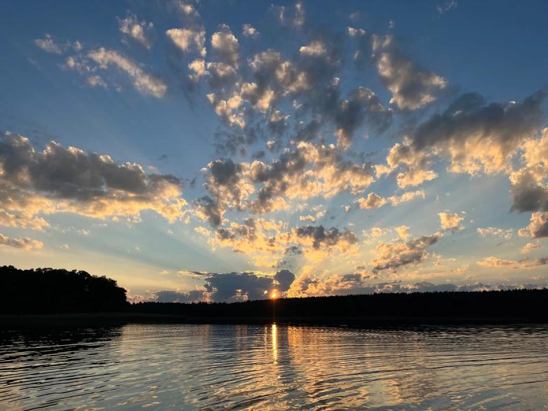 Strahlen der untergehenden Sonne hinter Wolken über dem Wasser.