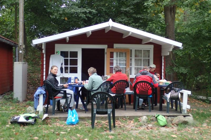 Gemeinsames Essen vor einer roten Holzhütte.