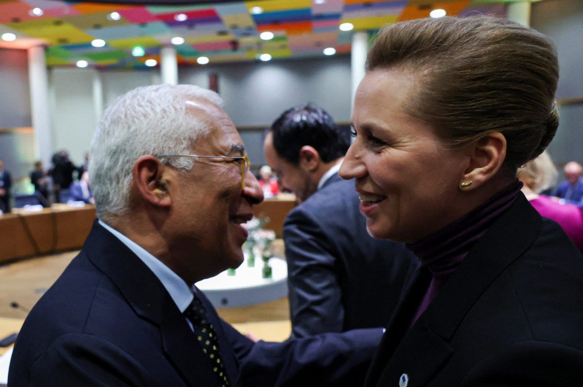 To personer i formelle antrekk smiler og snakker sammen ved et konferansebord i et sterkt opplyst møterom.