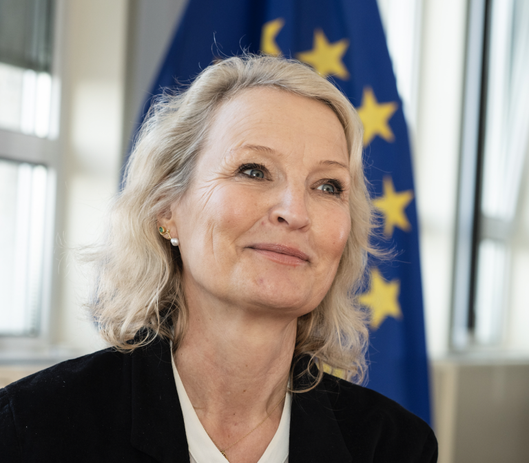 Smilende blond kvinne som ser opp, med EU-flagget i bakgrunnen.