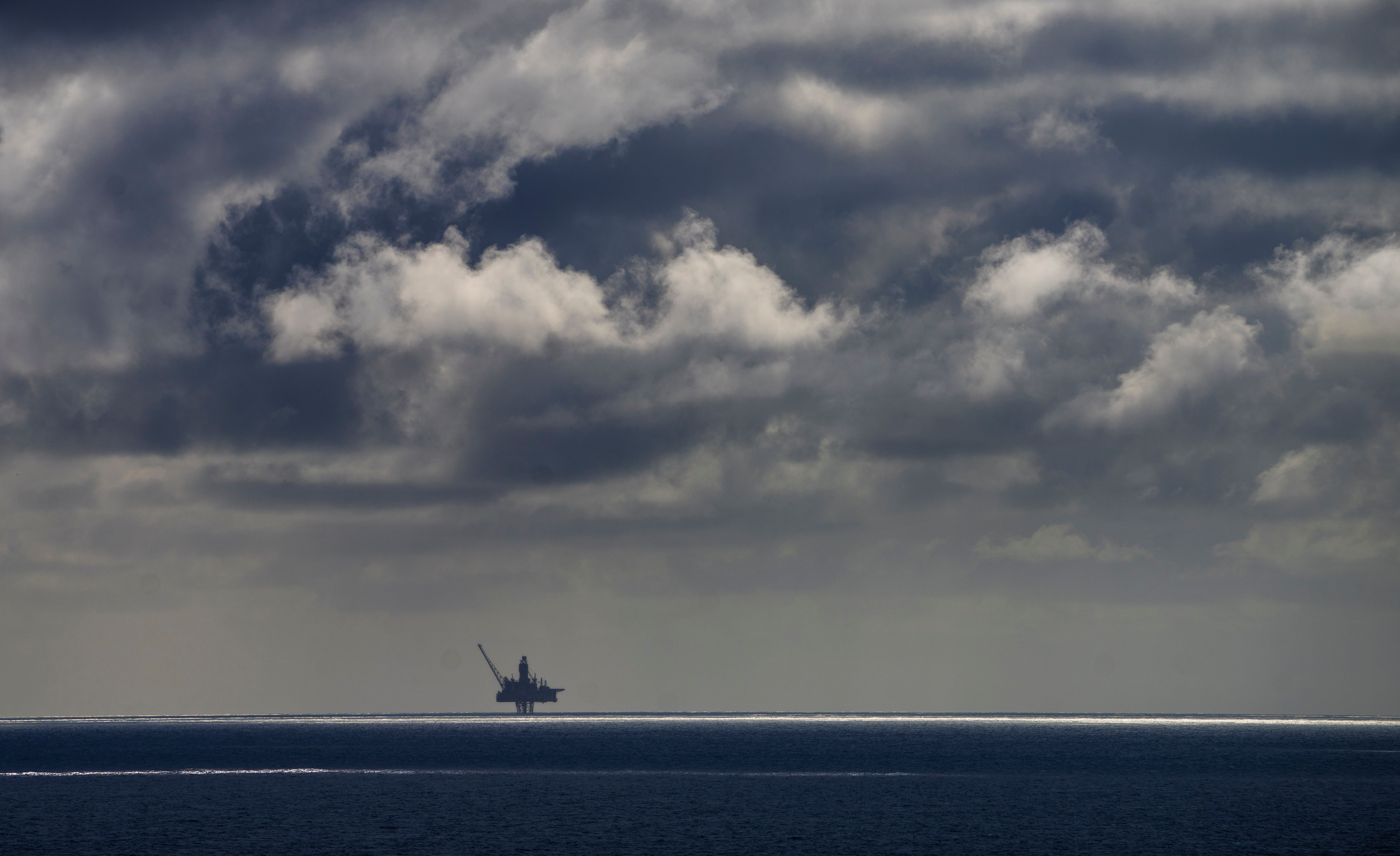 En offshore oljeplattform i silhuett mot en mørk, skyet himmel over havet.
