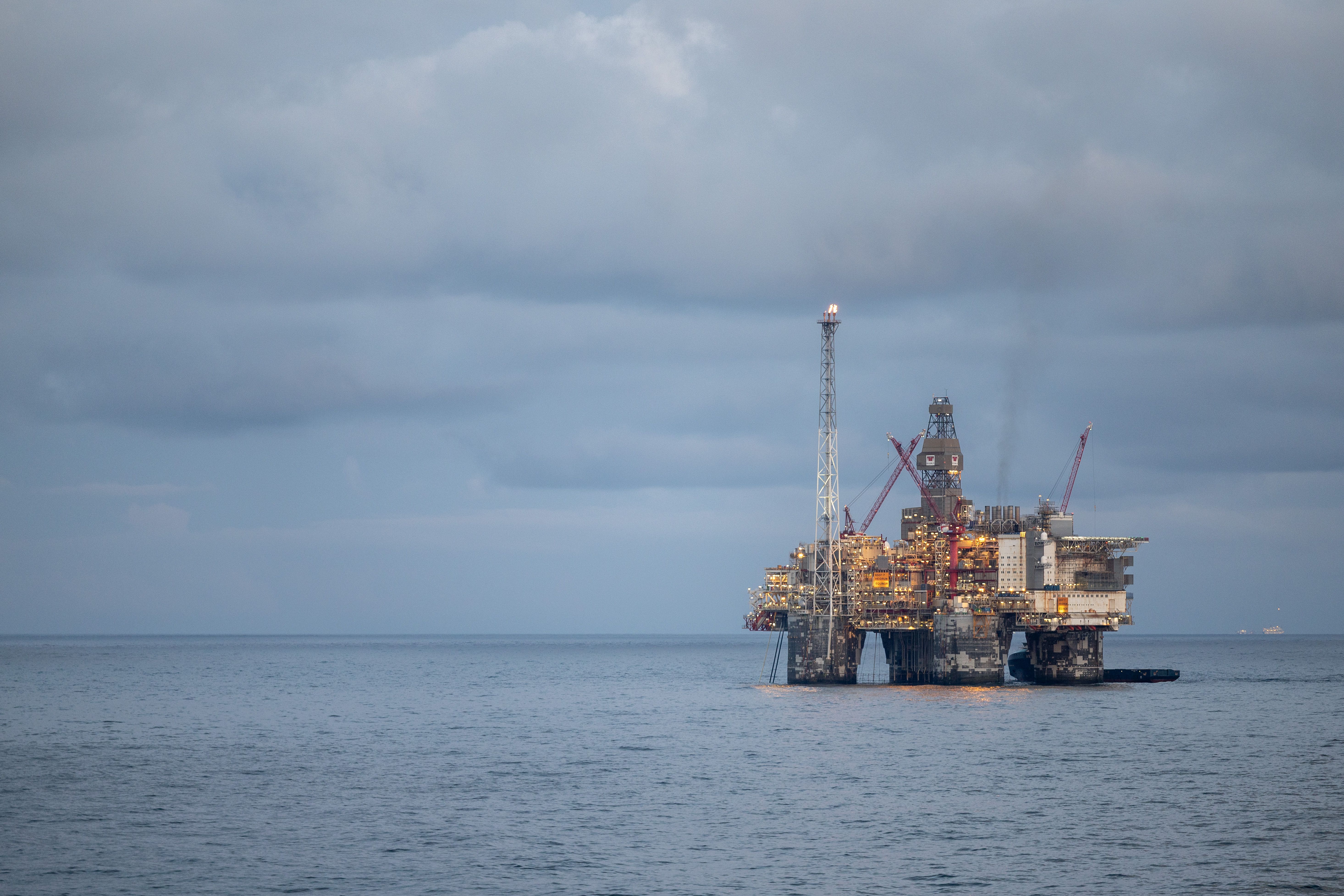 En opplyst oljeplattform til havs under en skyet himmel.
