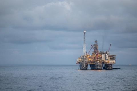 En opplyst oljeplattform til havs under en skyet himmel.