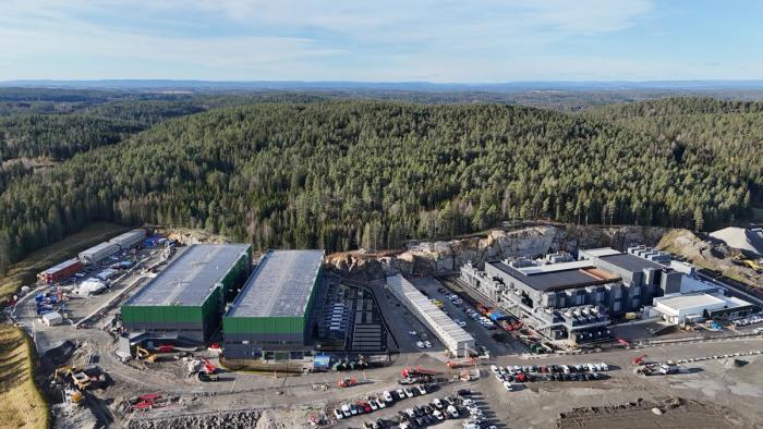 Flyfoto av et stort datasenterkompleks med grønne og grå bygninger, omgitt av tett skog.